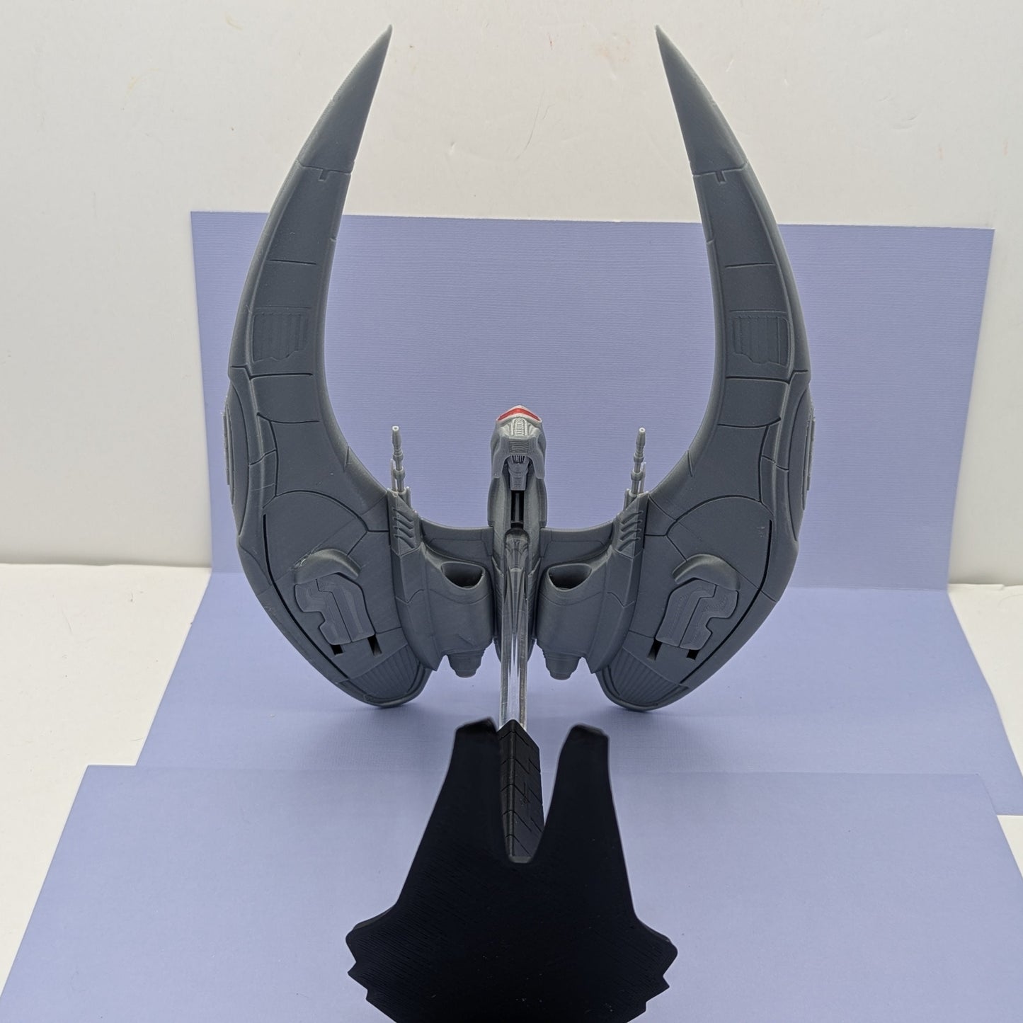 cylon model of a spaceship with large, curved wings on a reflective surface.