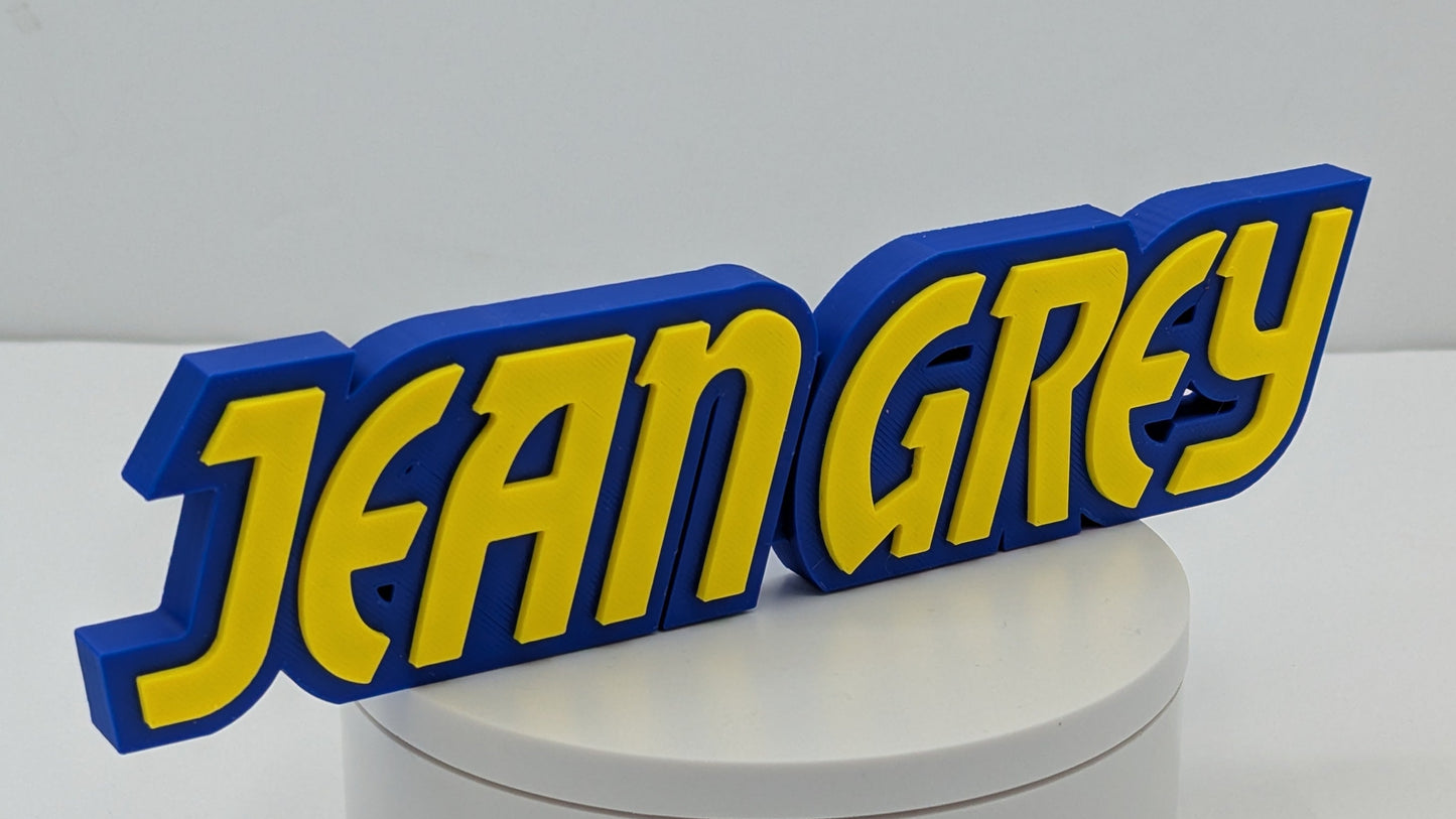 3D printed nameplate with 'JEAN GREY' in yellow and blue on a white base