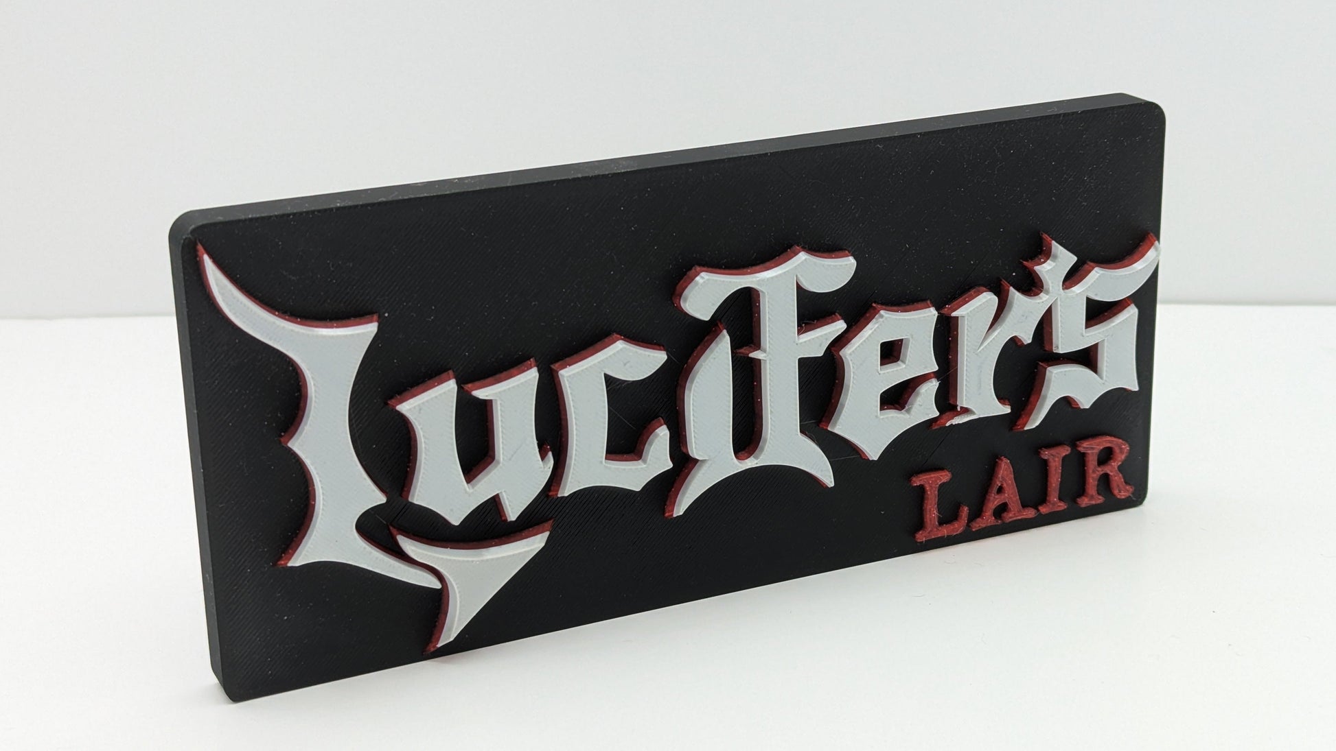 Decorative sign with 'Lucifer's Lair' text on a white background