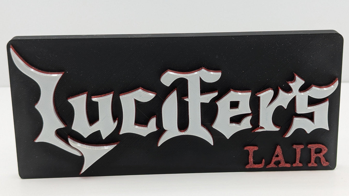 Black rectangular sign with 'Lucifer's Lair' in white and red text on a white background
