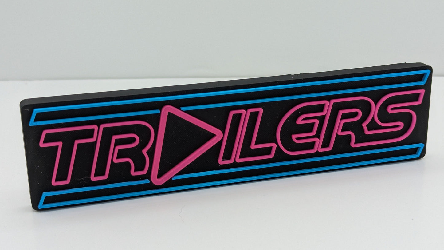 Rectangular sign with 'TRAILERS' text in pink and blue on a white background