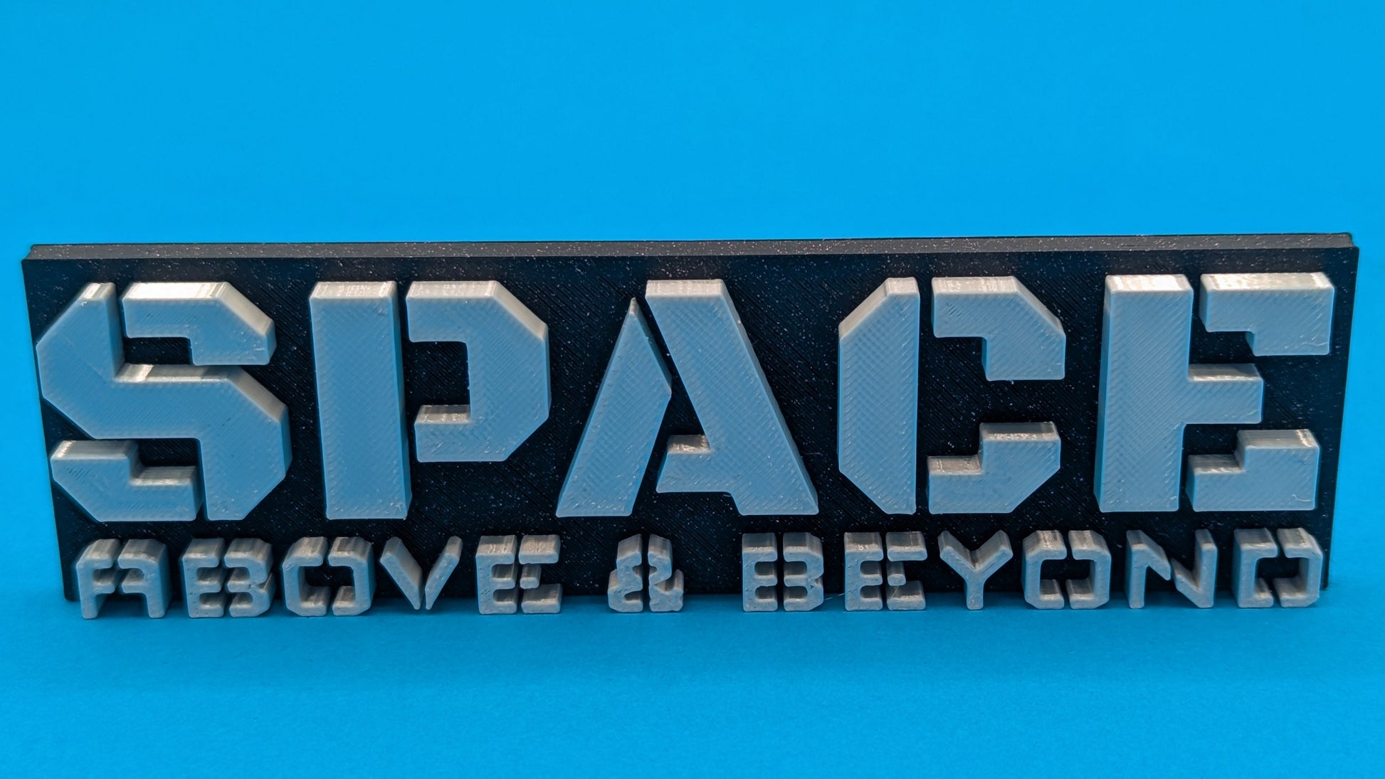 Metallic 'SPACE ABOVE & BEYOND' sign on a blue background