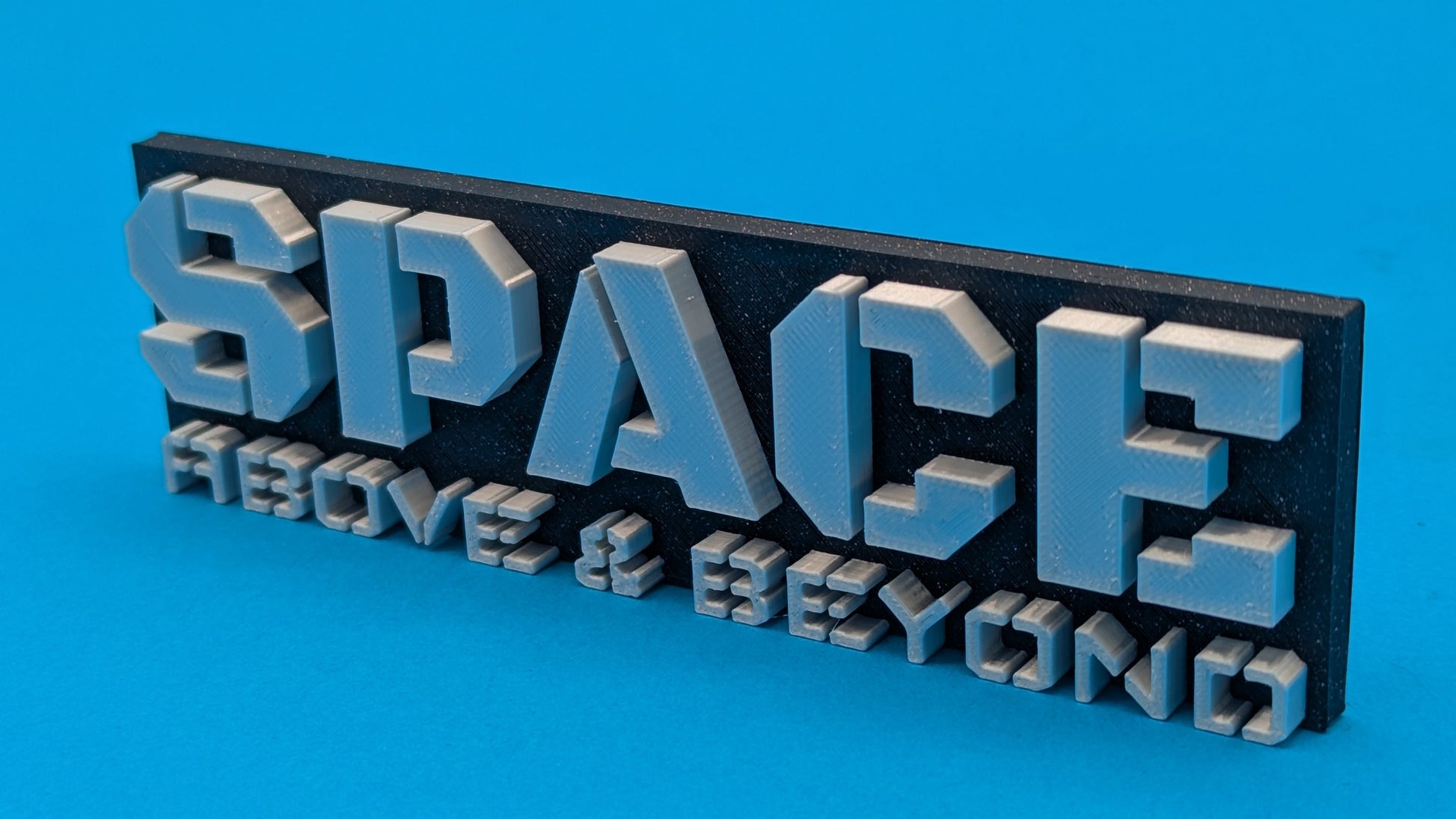 3D metal plaque with 'SPACE ABOVE & BEYOND' text on a blue background