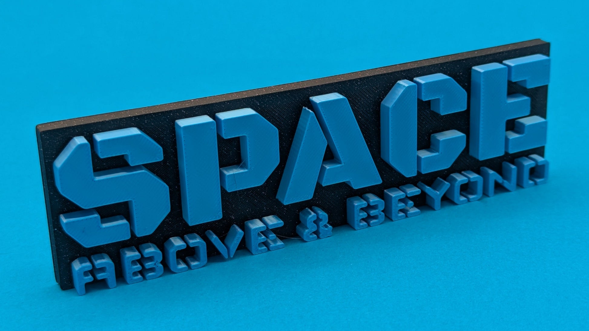 3D-printed 'SPACE ABOVE & BEYOND' sign on a blue background