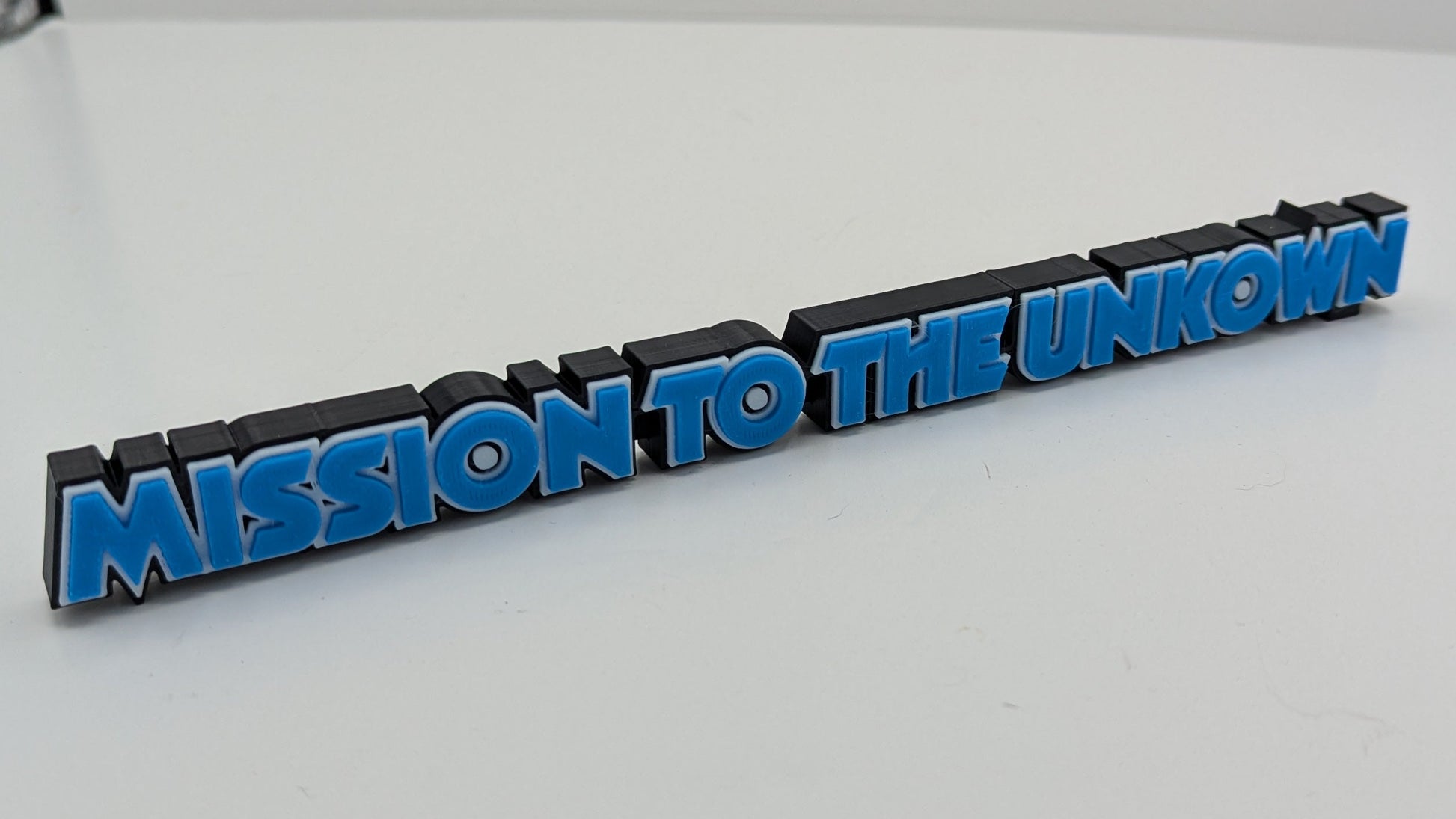 Text 'MISSION TO THE UNKNOWN' on a black and blue object against a white background