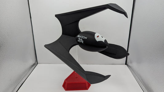 Black mask with white design and text on a red stand inside a display case.