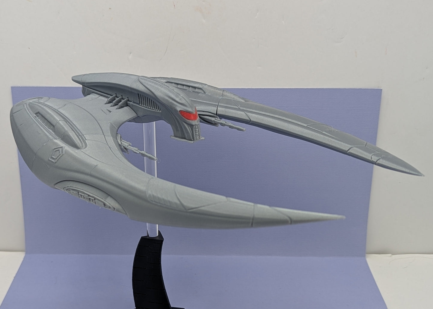 Model of a spaceship on a stand against a light purple background