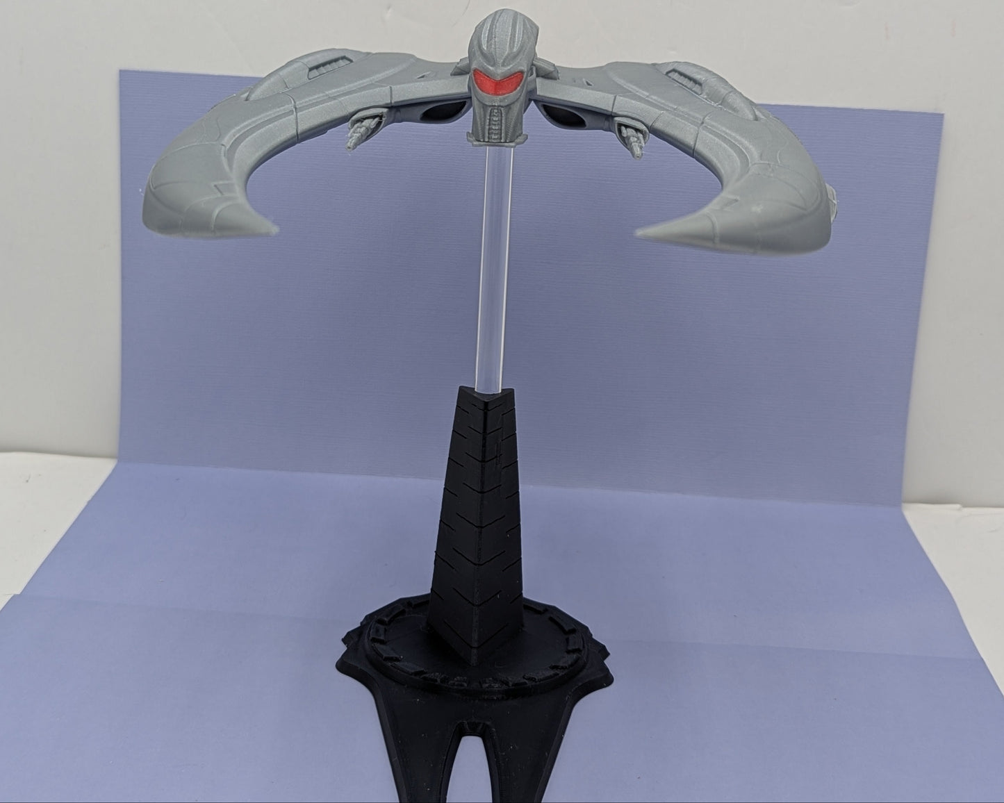 Gray weapon-like object on a stand against a light gray background
