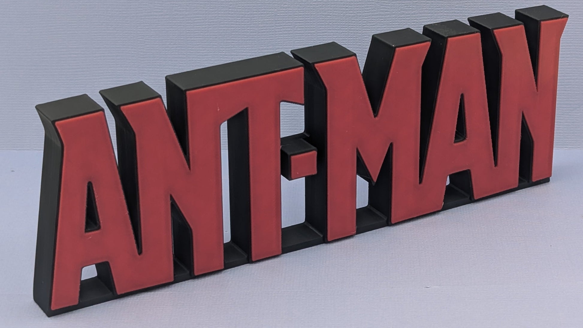 Red and black 'ANT-MAN' logo on a light gray background