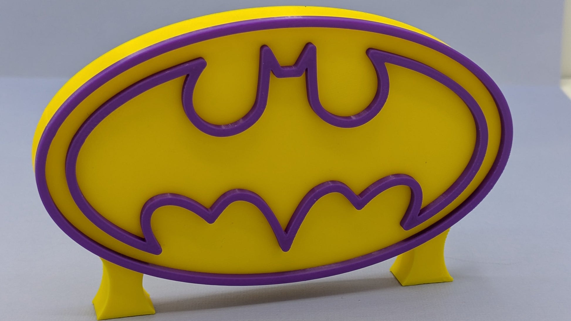 Yellow and purple Batgirl logo on a gray background