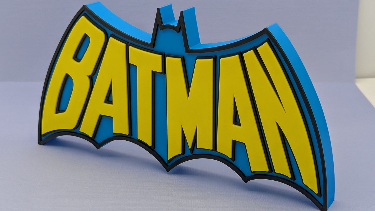 Batman logo with yellow letters and blue outline on a gray background