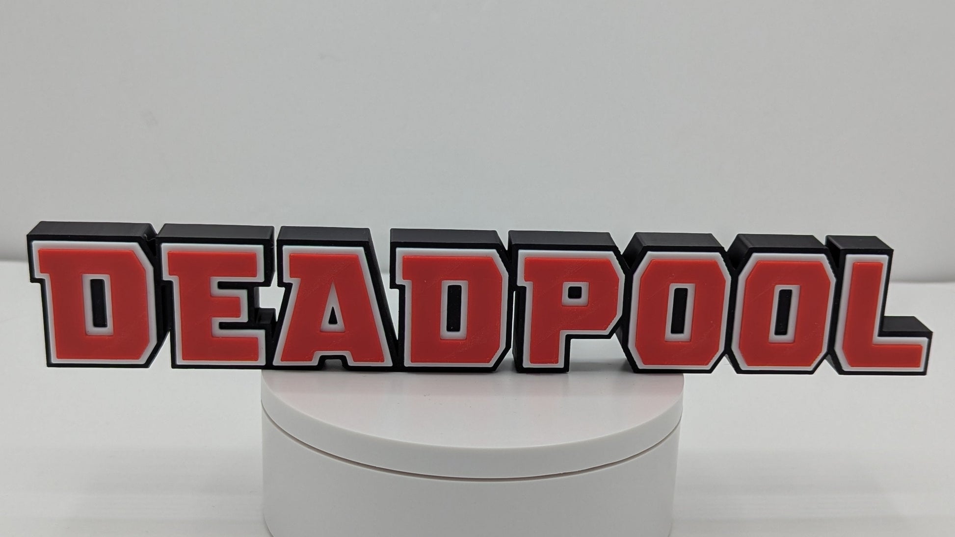 Round white box with 'DEADPOOL' logo on a gray background