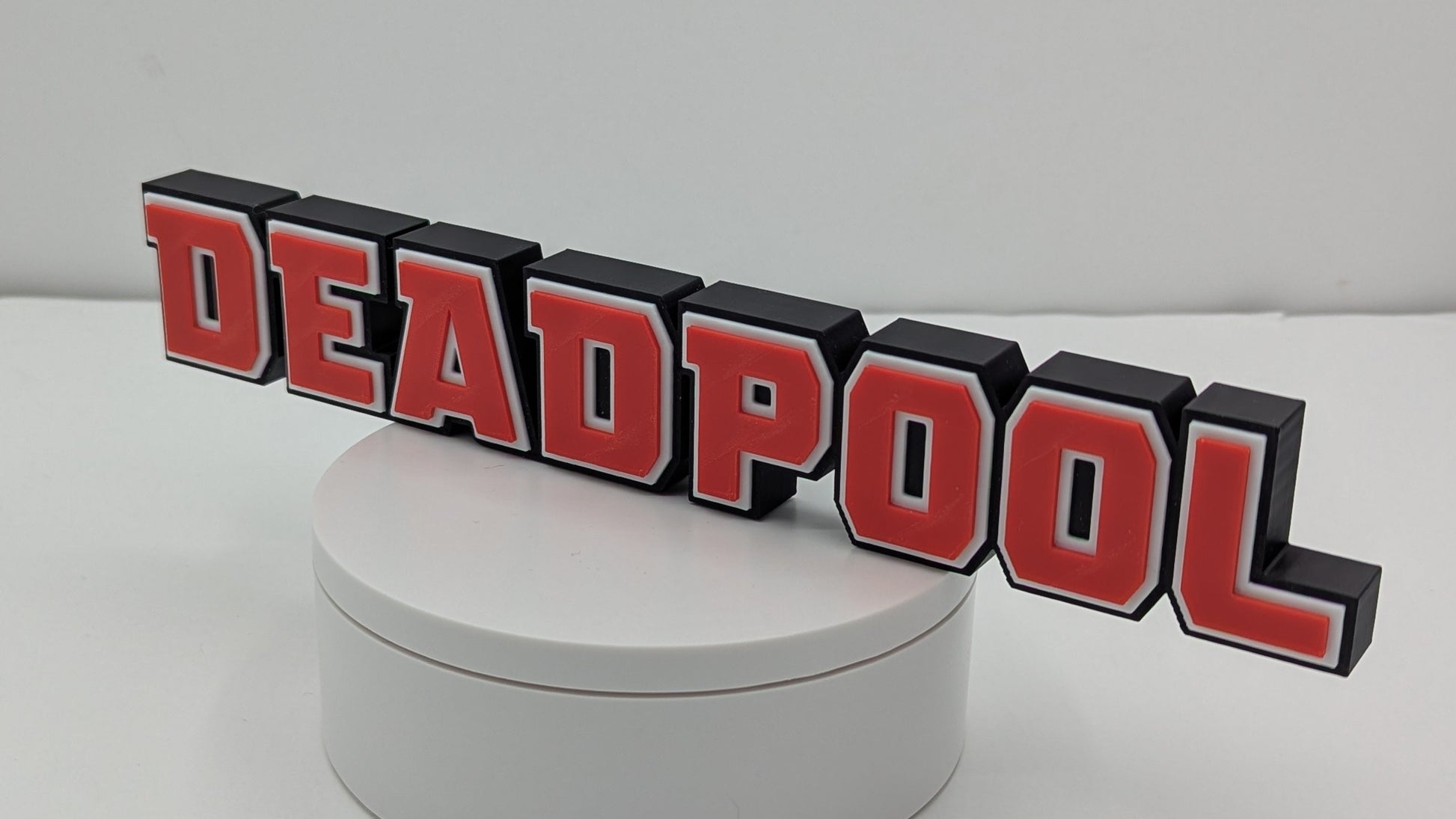 3D 'DEADPOOL' logo on a round white base with a gray background