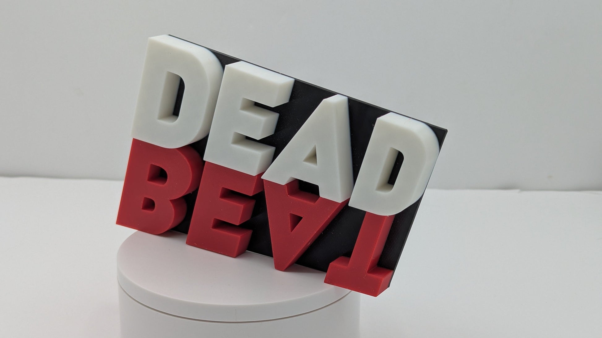 3D text sculpture spelling 'DEAD BEAT' on a white base with a gray background