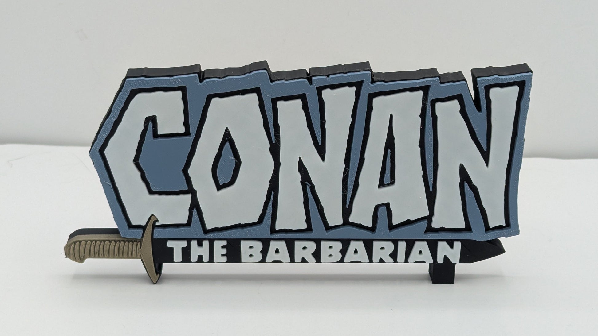 Decorative sign with 'Conan the Barbarian' text and a sword on a white background