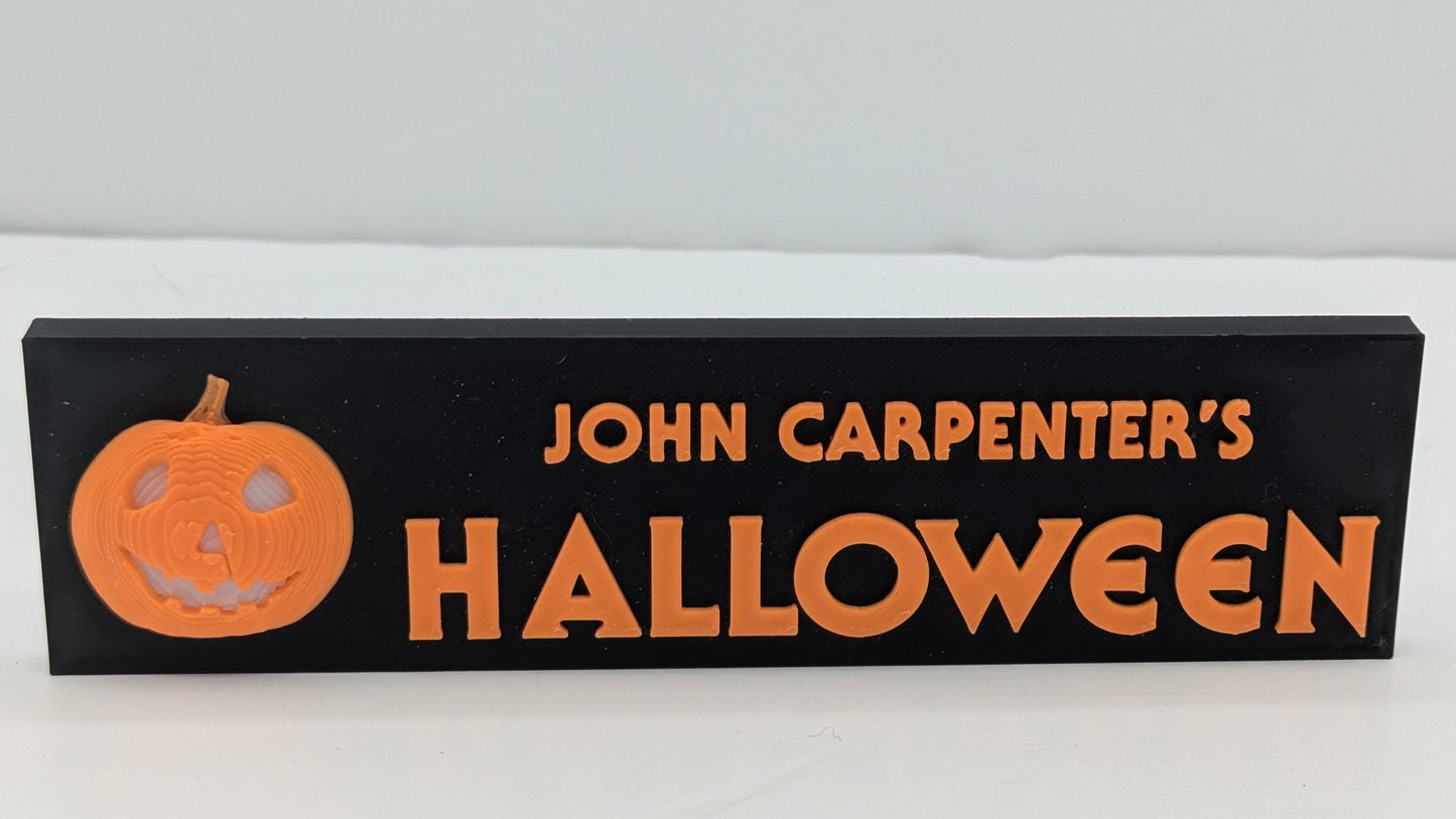 Wooden sign with 'John Carpenter's Halloween' and a pumpkin graphic on a white background