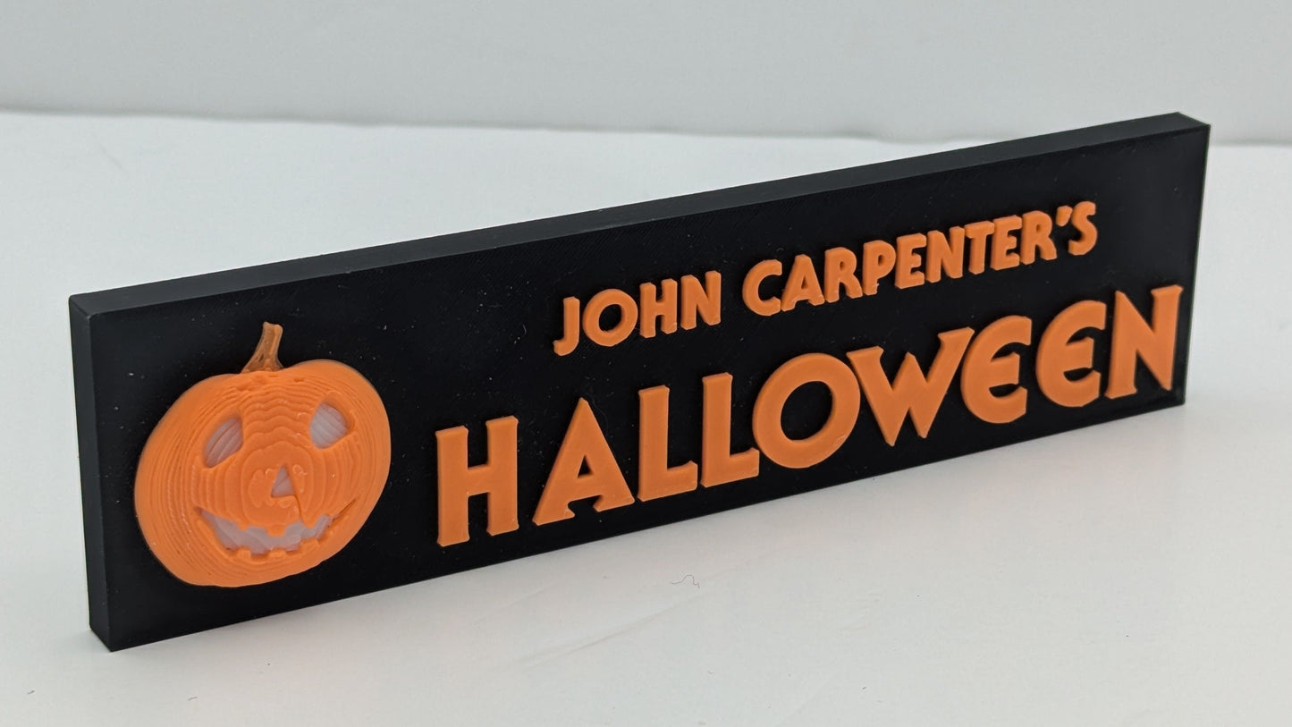 Decorative sign for 'John Carpenter's Halloween' with a pumpkin graphic on a white background