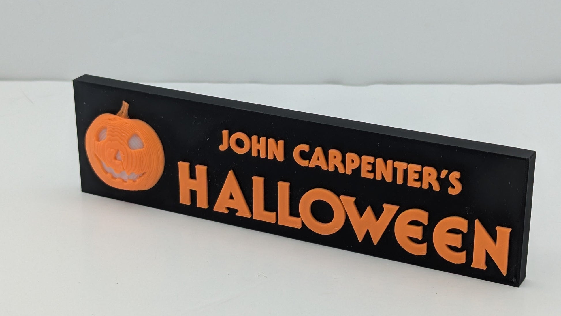 Halloween-themed sign with 'John Carpenter's Halloween' and a pumpkin on a white background