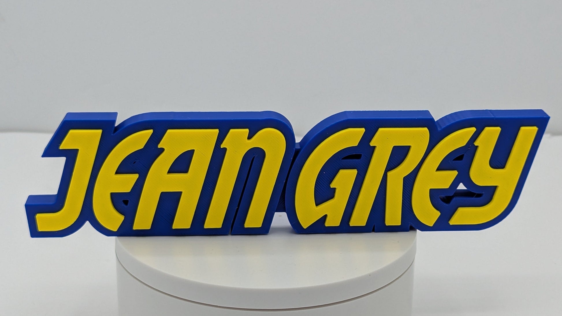 3D printed nameplate with 'JEAN GREY' in yellow and blue on a white base.