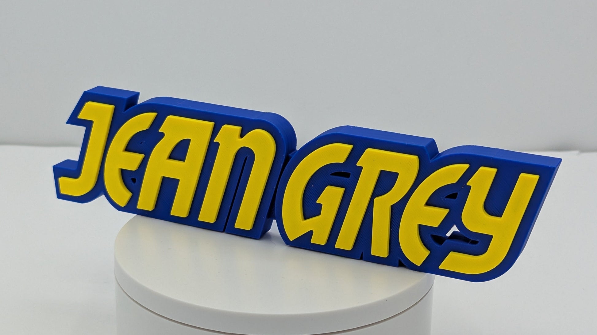 3D printed nameplate with 'JEAN GREY' in yellow and blue on a white base.