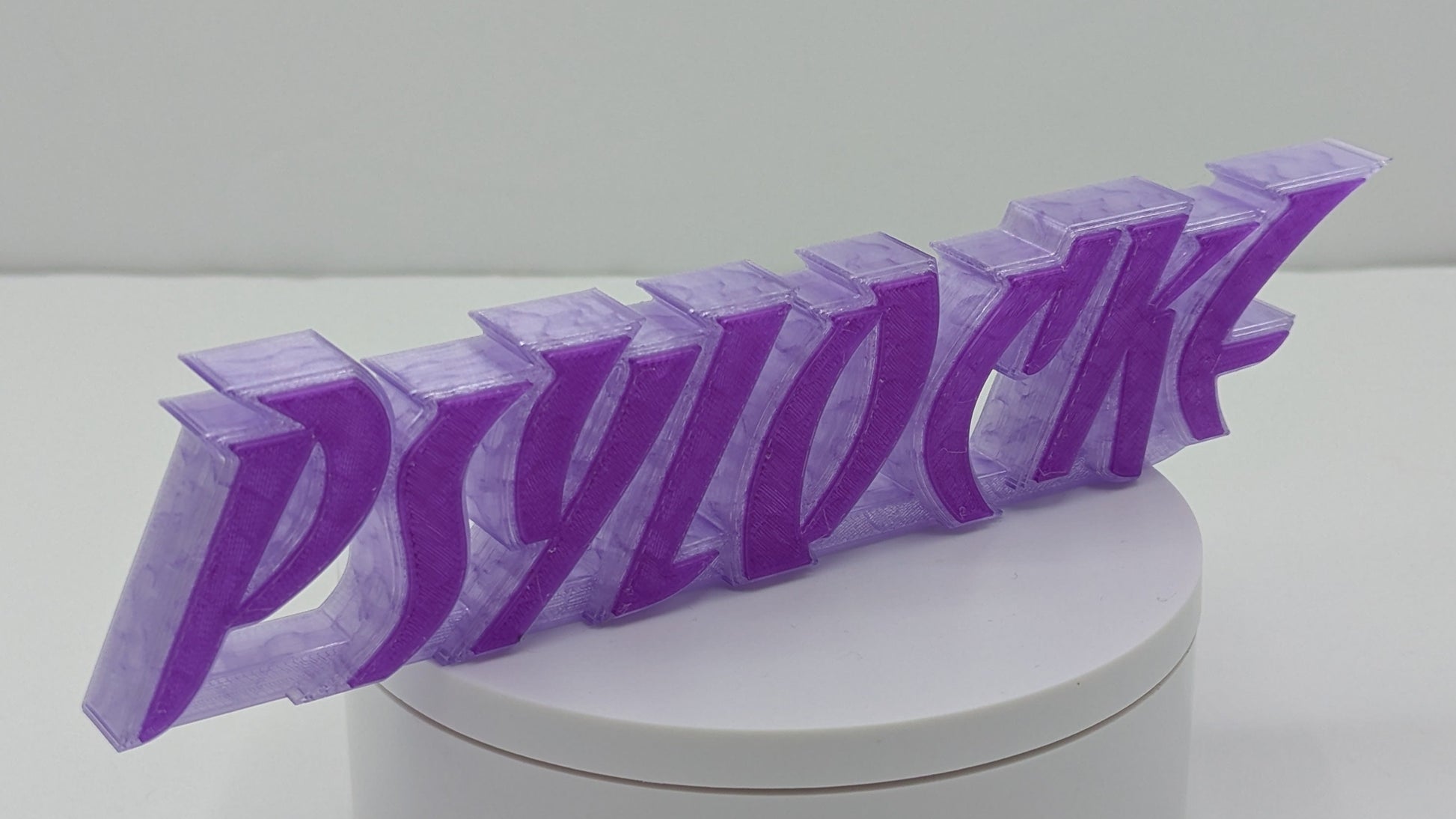 3D-printed 'PSYLOCKE' logo on a white cylindrical base with a white background