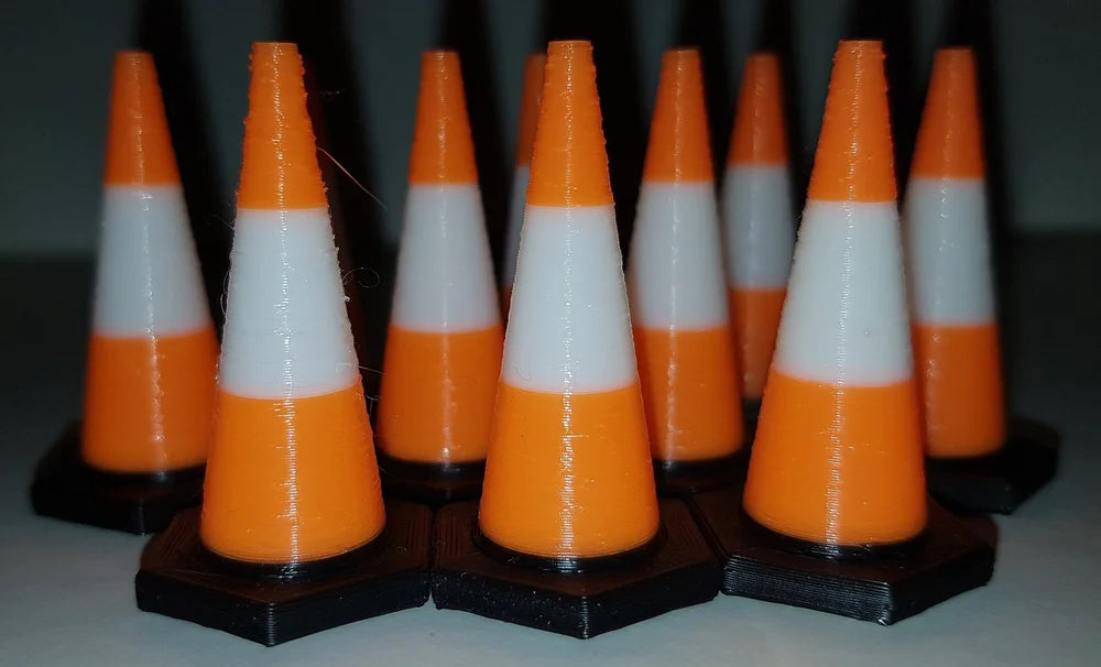 Model traffic cones with orange and white stripes on a reflective surface.